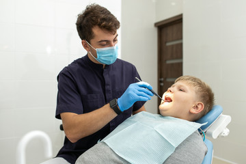 Dentist in clinic examines teeths of young boy