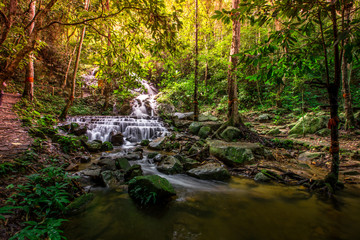 Natural blurred background of waterfalls, fast-flowing currents and water droplets from the wind blowing among the rocks and surrounded by big trees, spontaneous beauty