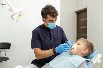 A young boy is lying on the dental chair and is being examinated by a doctor