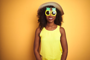 African american woman wearing funny pineapple sunglasses over isolated yellow background with a happy and cool smile on face. Lucky person.