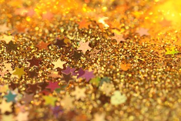 Christmas and New Year background. Stars and golden glitter on a blurry gold background.Golden shiny macro texture.Winter holidays background