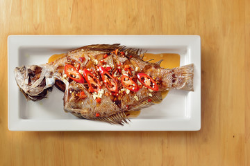 food background of Thai style deep fried whole seabass with garlic and chili in fish sauce on wooden table