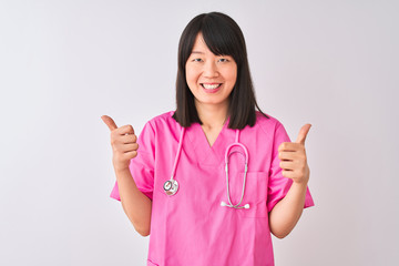 Young beautiful Chinese nurse woman wearing stethoscope over isolated white background success sign doing positive gesture with hand, thumbs up smiling and happy. Cheerful expression