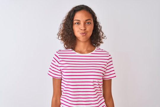 Young brazilian woman wearing pink striped t-shirt standing over isolated white background puffing cheeks with funny face. Mouth inflated with air, crazy expression.