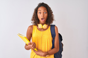 Brazilian student woman wearing backpack holding notebook over isolated white background scared in...