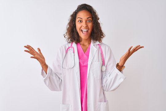 Young brazilian doctor woman wearing stethoscope standing over isolated white background celebrating crazy and amazed for success with arms raised and open eyes screaming excited. Winner concept
