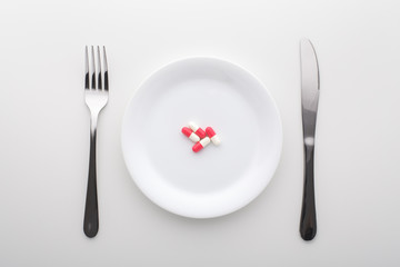 Fototapeta na wymiar Capsule pills on white plate with fork and knife