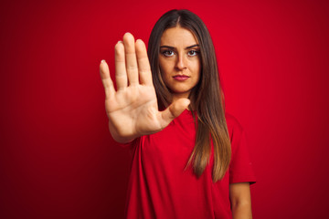 Young beautiful woman wearing t-shirt standing over isolated red background doing stop sing with palm of the hand. Warning expression with negative and serious gesture on the face. - obrazy, fototapety, plakaty