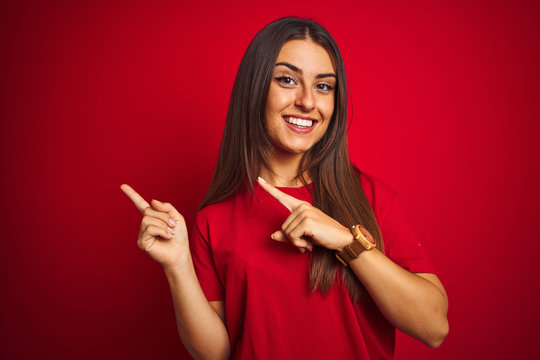 Young beautiful woman wearing t-shirt standing over isolated red background smiling and looking at the camera pointing with two hands and fingers to the side.