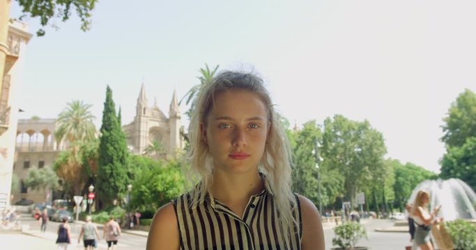 Young Blonde Pretty Woman in a Smart Stripe Shirt standing in the Lovely Spanish Palma City in Front of a Water Fountain. Gap Year Girl Student in Europe.
