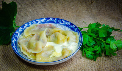 varenyky pierogi dumplings ravioli with wild strawberry Ukrainian traditional food in a plate with an ornament and a wooden spoon with greens parsley and red currants
