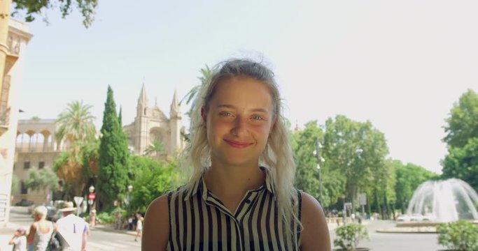 Young Blonde Pretty Woman in a Smart Stripe Shirt standing in the Lovely Spanish Palma City in Front of a Water Fountain. Gap Year Girl Student in Europe.Smiling Enjoying the sun