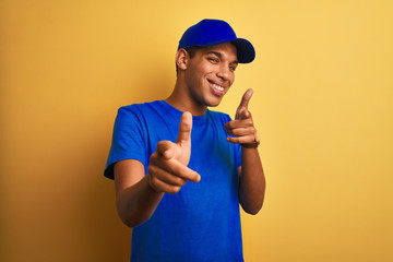 Young handsome arab delivery man standing over isolated yellow background pointing fingers to camera with happy and funny face. Good energy and vibes.