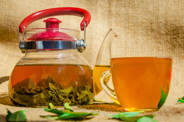 glass teapot and cup of green tea or black tea with fresh leaves on the back of a traditional...
