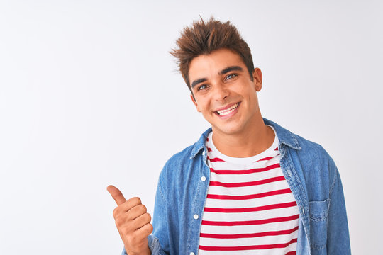 Young handsome man wearing striped t-shirt and denim shirt over isolated white background smiling with happy face looking and pointing to the side with thumb up.