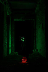 Man in scary led mask sitting next to halloween pumpkin glowing from inside in dark passage
