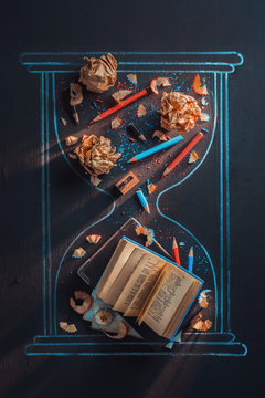 Chalk hourglass drawing with books, crumpled paper, and pencils. Writing creative process conceptual flat lay on a black background.