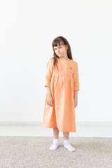 Beautiful little girl in a peach dress posing against a white wall. The concept of children's designer clothes.