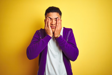 Young brazilian man wearing purple sweatshirt standing over isolated yellow background rubbing eyes for fatigue and headache, sleepy and tired expression. Vision problem