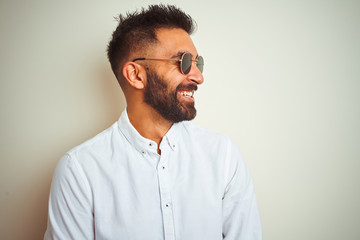 Handsome indian buinessman wearing shirt and sunglasses over isolated white background looking away...