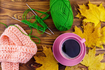 Cup of coffee, ball of yarn, knitting, knitted scarf and yellow maple leaves on wooden table. Autumn still life