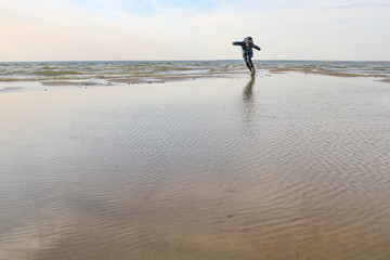 Preschool boy spinning alone in the sea surf on a cold autumn day. Copy space