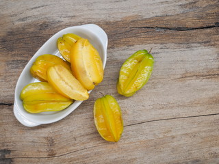Top view a group of ripe yellow Star Fruit (Carambola) in white dish on wood texture background.