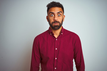 Obraz premium Young indian man wearing red elegant shirt standing over isolated grey background puffing cheeks with funny face. Mouth inflated with air, crazy expression.