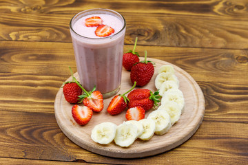 Glass of fresh smoothie of strawberry and banana on a wooden table