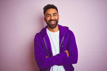 Fototapeta premium Young indian man wearing purple sweatshirt standing over isolated pink background happy face smiling with crossed arms looking at the camera. Positive person.