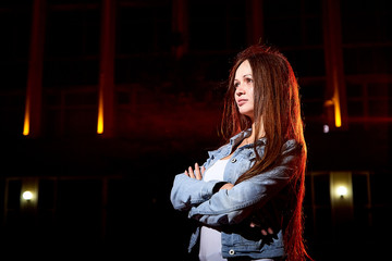 Portrait of young brunette woman with long hair on a city street at night and colored lights