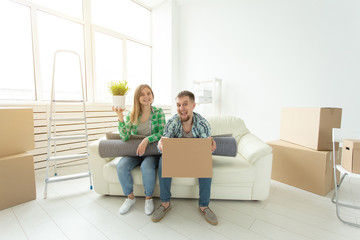 Fototapeta na wymiar Cheerful joyful young couple charming girl and handsome man holding a box with things and a pot with a plant while moving to a new apartment. Housewarming and mortgage concept.