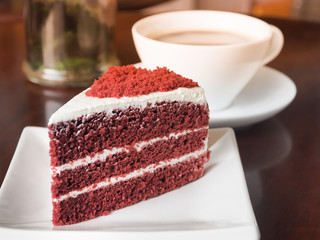 Slice of red velvet cake on a white plate. Close up of red velvet chocolate cake with a cup of hot...