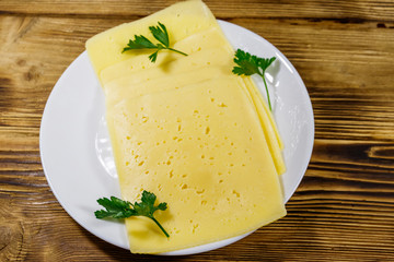 Slices of cheese in a plate on wooden table. Top view
