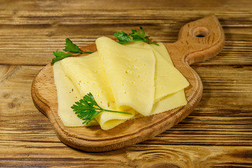 Slices of cheese on cutting board on wooden table