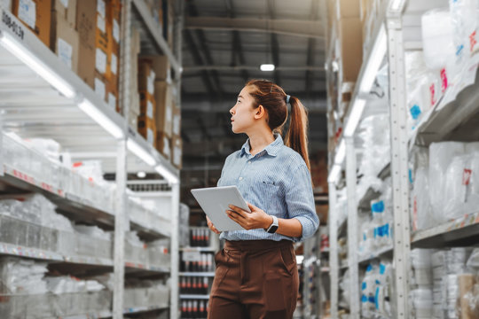 Asian woman worker working with digital tablet checking boxes Logistic import and export supplies packages in Warehouse , Logistics concept