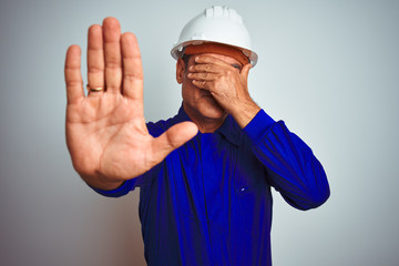 Handsome middle age worker man wearing uniform and helmet over isolated white background covering eyes with hands and doing stop gesture with sad and fear expression. Embarrassed and negative concept.