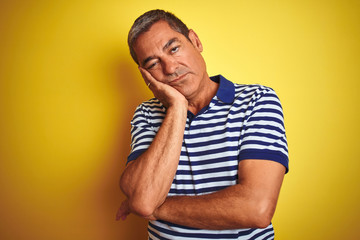 Handsome middle age man wearing striped polo standing over isolated yellow background thinking looking tired and bored with depression problems with crossed arms.