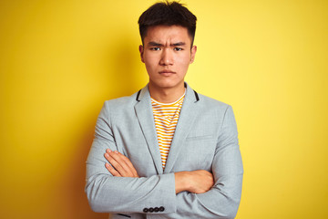 Young asian chinese businessman wearing jacket standing over isolated yellow background skeptic and nervous, disapproving expression on face with crossed arms. Negative person.