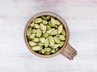 Spice Green cardamom (Elettaria cardamomum) in a clay cup on a brown wooden background