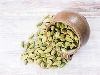 Spice Green cardamom (Elettaria cardamomum) scattered from a clay cup on a brown wooden background