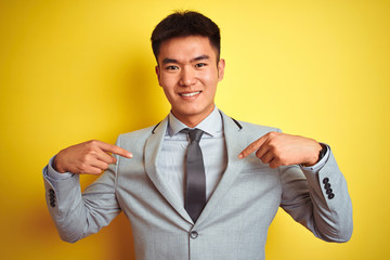 Asian chinese businessman wearing suit and tie standing over isolated yellow background looking confident with smile on face, pointing oneself with fingers proud and happy.