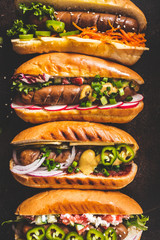 Hot dogs with different toppings on dark background, top view. Fast food concept.