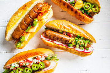Hot dogs with different toppings on white wooden background, top view. Fast food concept.