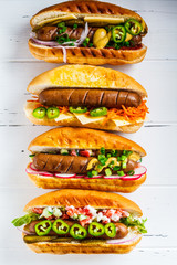 Hot dogs with different toppings on white wooden background, top view. Fast food concept.