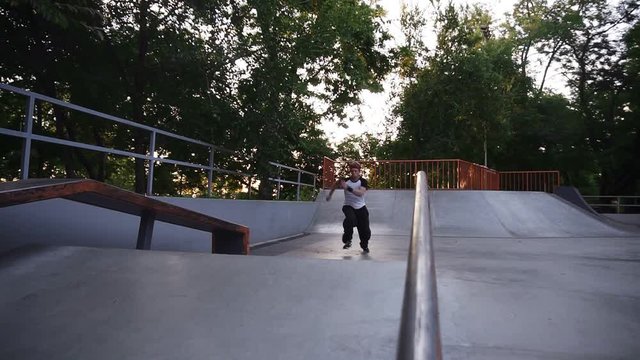 Low angle footage of a blonde, active guy making somersault before sliding and running from the ramp in the outdoors skate park. Slow motion