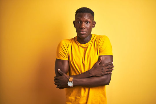 Young african american man wearing casual t-shirt standing over isolated yellow background shaking and freezing for winter cold with sad and shock expression on face