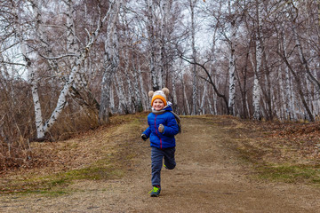cheerful boy in a warm jacket and hat runs through the woods