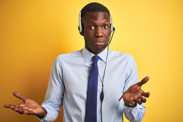 African american operator man working using headset over isolated yellow background clueless and...