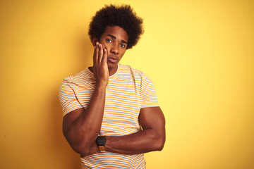 Fototapeta na wymiar American man with afro hair wearing striped t-shirt standing over isolated yellow background thinking looking tired and bored with depression problems with crossed arms.